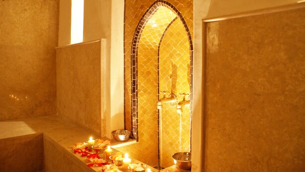 Un baño con pared de azulejos, una bañera y un estante con un tazón y una vela.