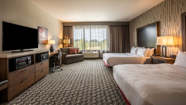 A hotel room with a flat-screen TV, two beds, a desk with a lamp, a sofa, and a large window with curtains. - Holiday Inn Portland West - Hillsboro by IHG (Hillsboro)