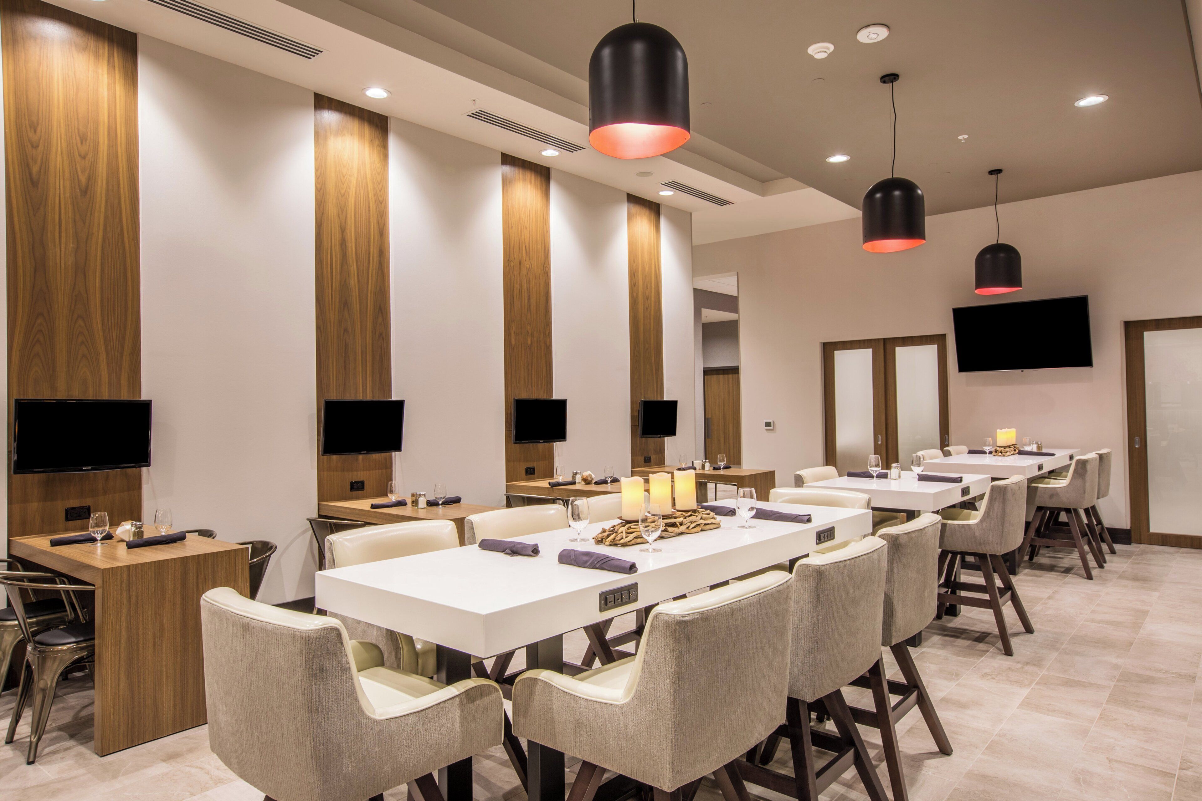 A hotel dining area with multiple tables, chairs, and pendant lighting.