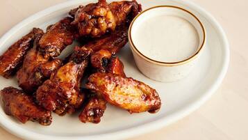 A plate of glazed chicken wings with a side of dipping sauce.