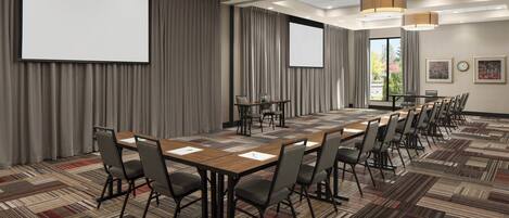 A conference room with a long table, chairs, a projector screen, and a carpeted floor.