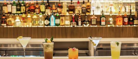 A bar with a variety of liquor bottles in the background and four different cocktails in the foreground.