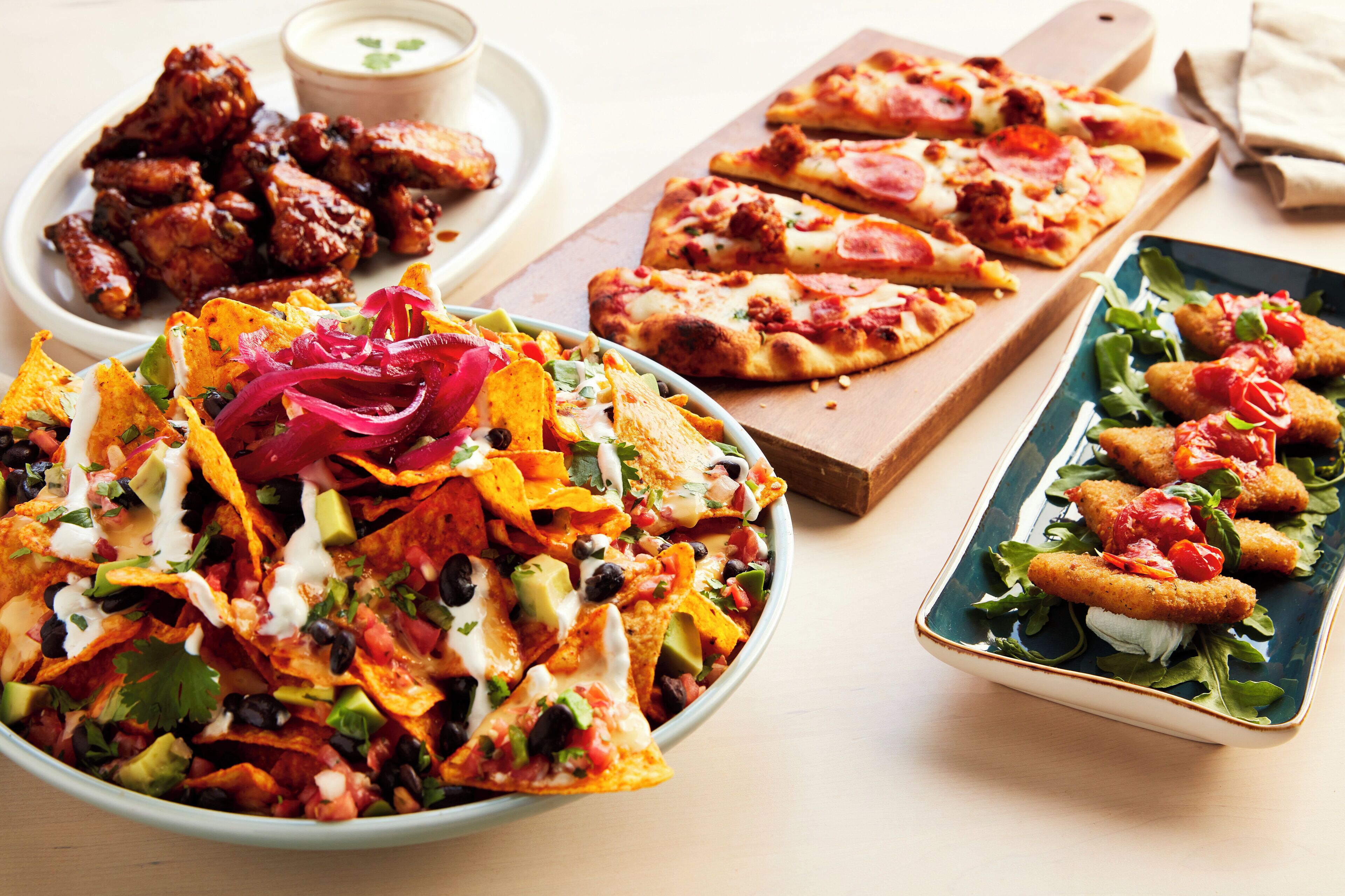 Eine Auswahl an Gerichten, darunter Nachos, Pizza und Chicken Wings, auf einem Tisch.