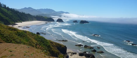 Un paisaje costero con una playa arenosa, costa rocosa y una ladera cubierta de bosque.
