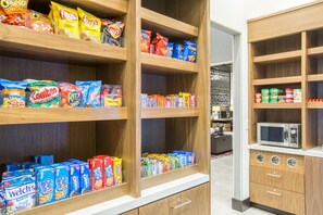 Een snackvak met verschillende pakjes en zakjes snacks en een magnetron op het aanrecht.