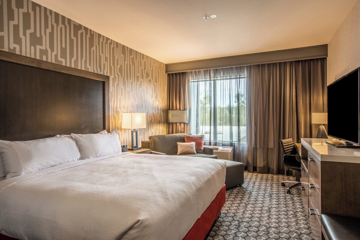Een hotelkamer met een groot bed, een bureau, een stoel, een televisie en een raam met gordijnen.