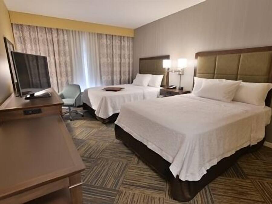 A hotel room with two beds, a desk, a chair, a TV, and a window with curtains.