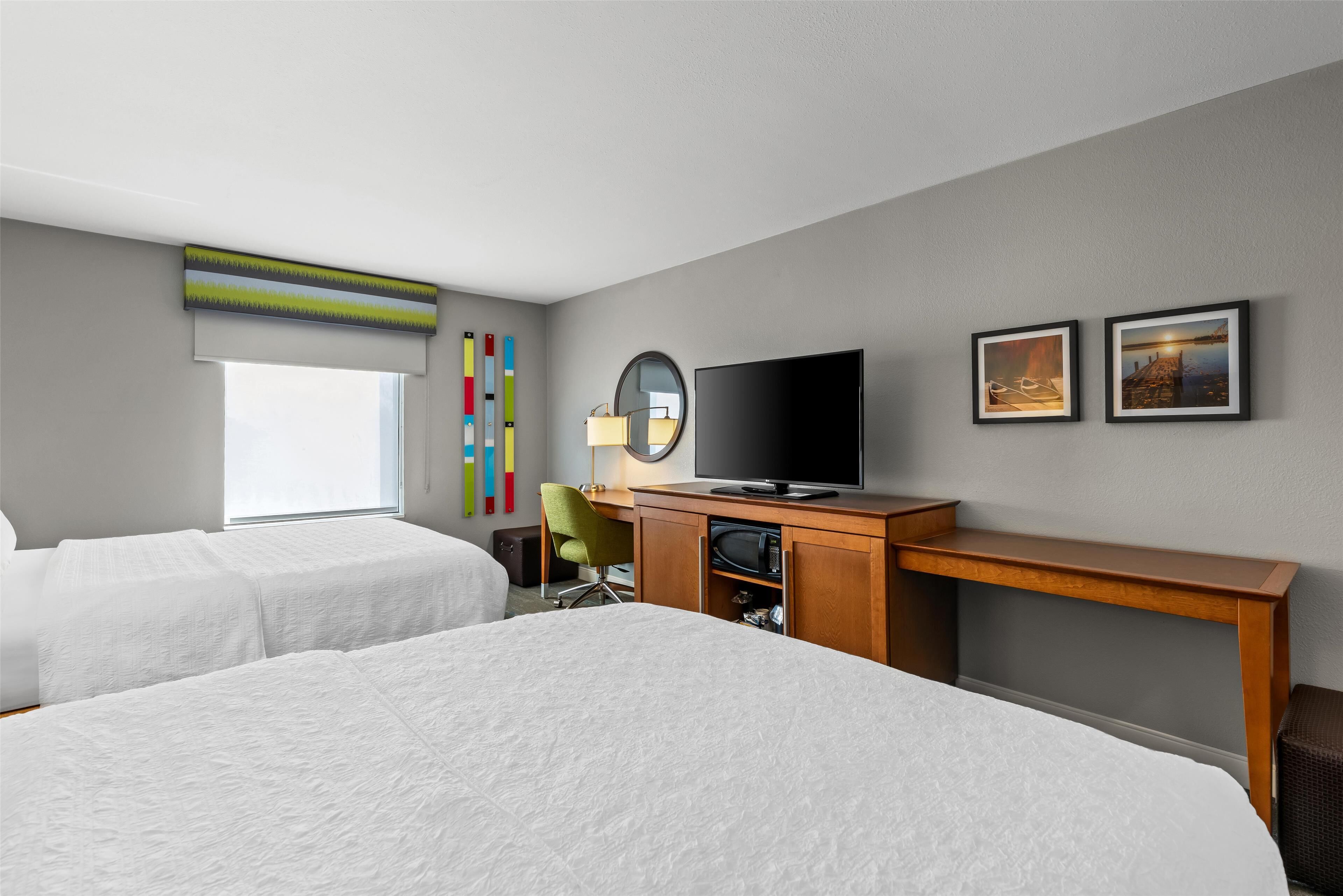 A hotel room with two beds, a desk with a TV, a chair, and a window.
