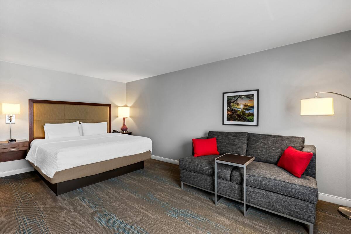 A hotel room with a bed, a sofa, a small table, and a painting on the wall.