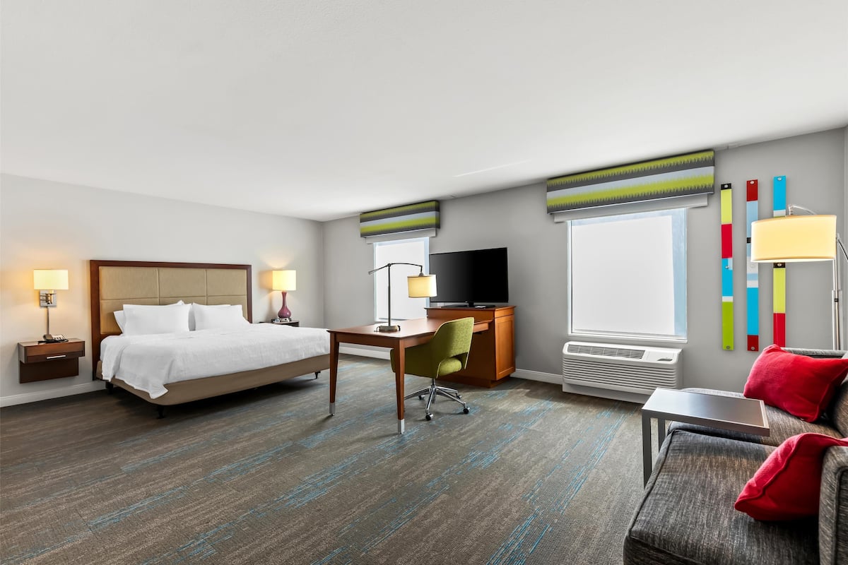 A hotel room with a bed, desk, chair, TV, and a window with blinds.