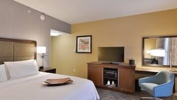 A hotel room with a bed, a desk with a TV, a chair, and a framed picture on the wall.