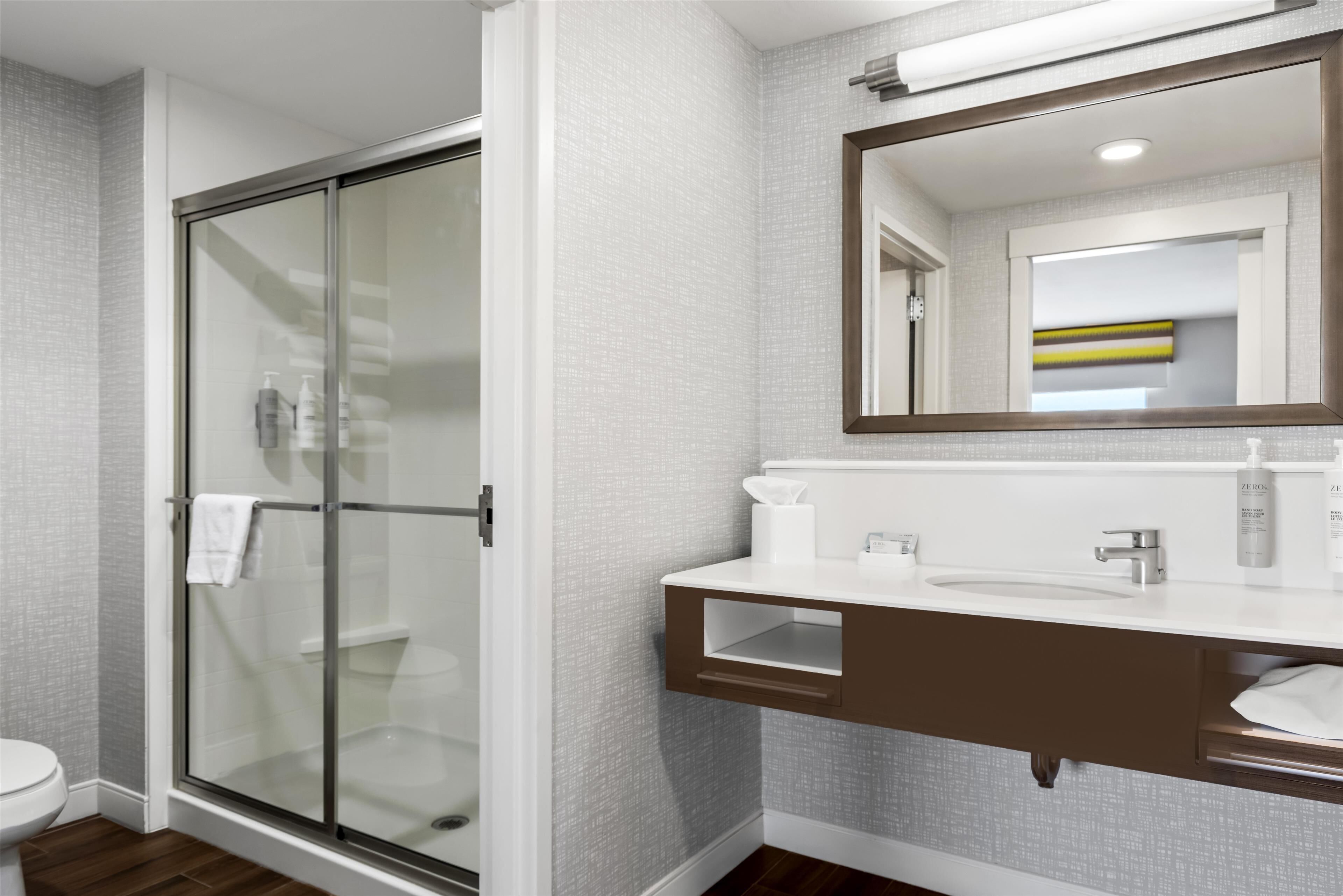 Une salle de bain moderne avec une douche à parois de verre, un lavabo blanc et un miroir au-dessus du meuble-lavabo.