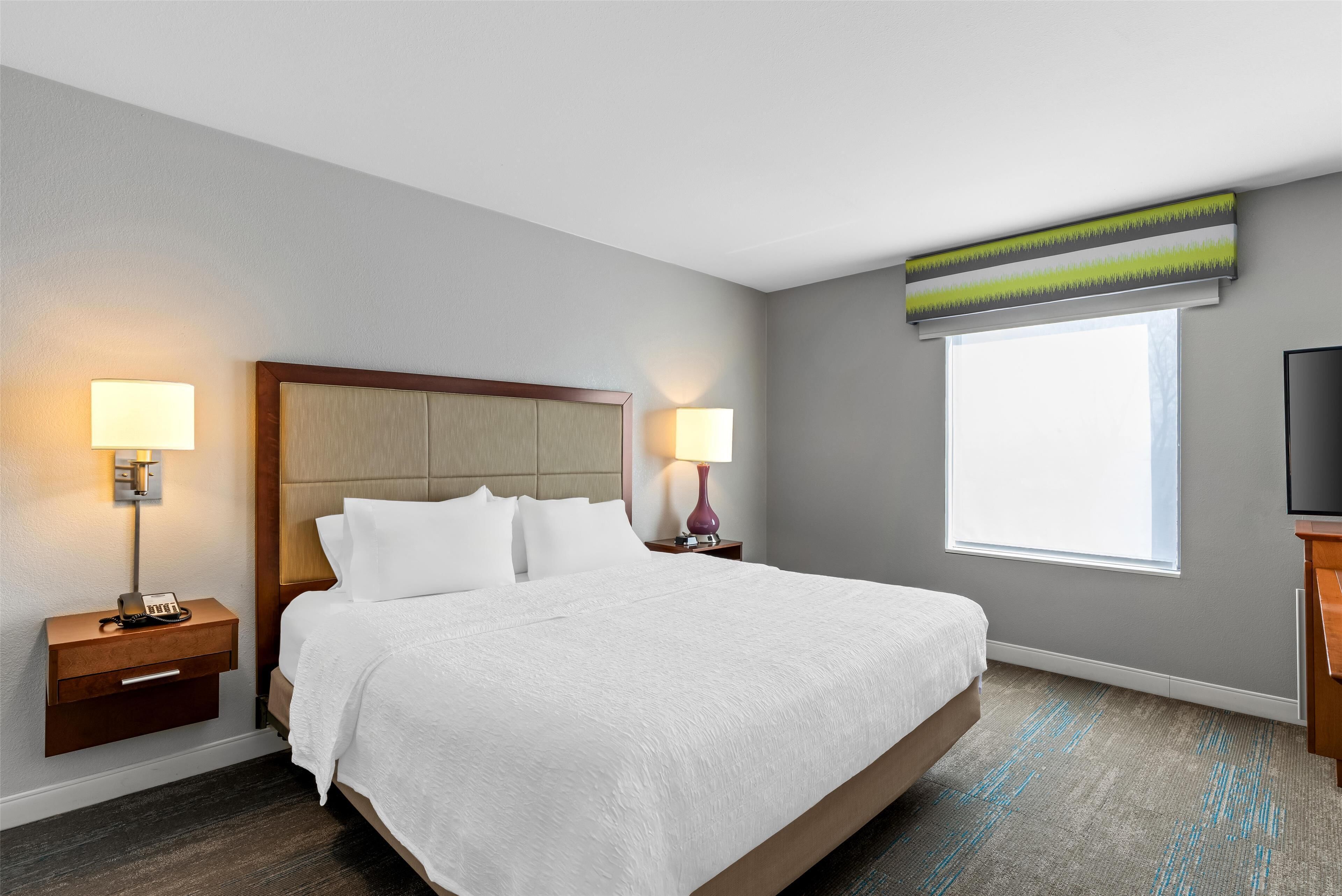 A hotel room with a large bed, two bedside tables with lamps, a television, and a window with a view.