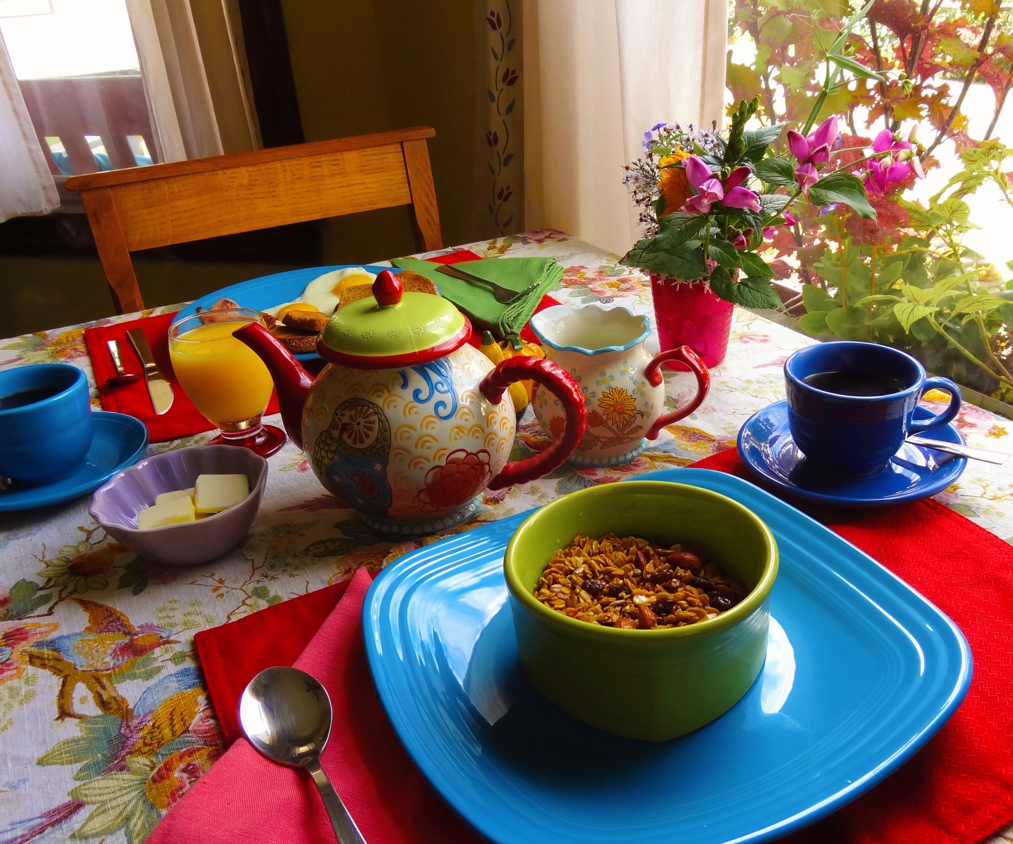A dining table with a floral tablecloth, a wooden chair, and various dishes and utensils.