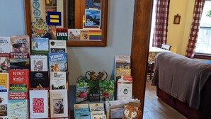 A wooden desk with a variety of books and pamphlets, a small tiger figurine, and a mirror reflecting the room.