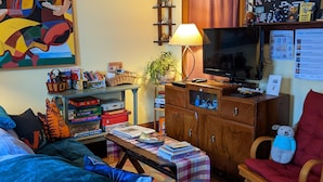 A cozy living room with a television, books, and a comfortable couch. - The One Cat B&B (Brattleboro)