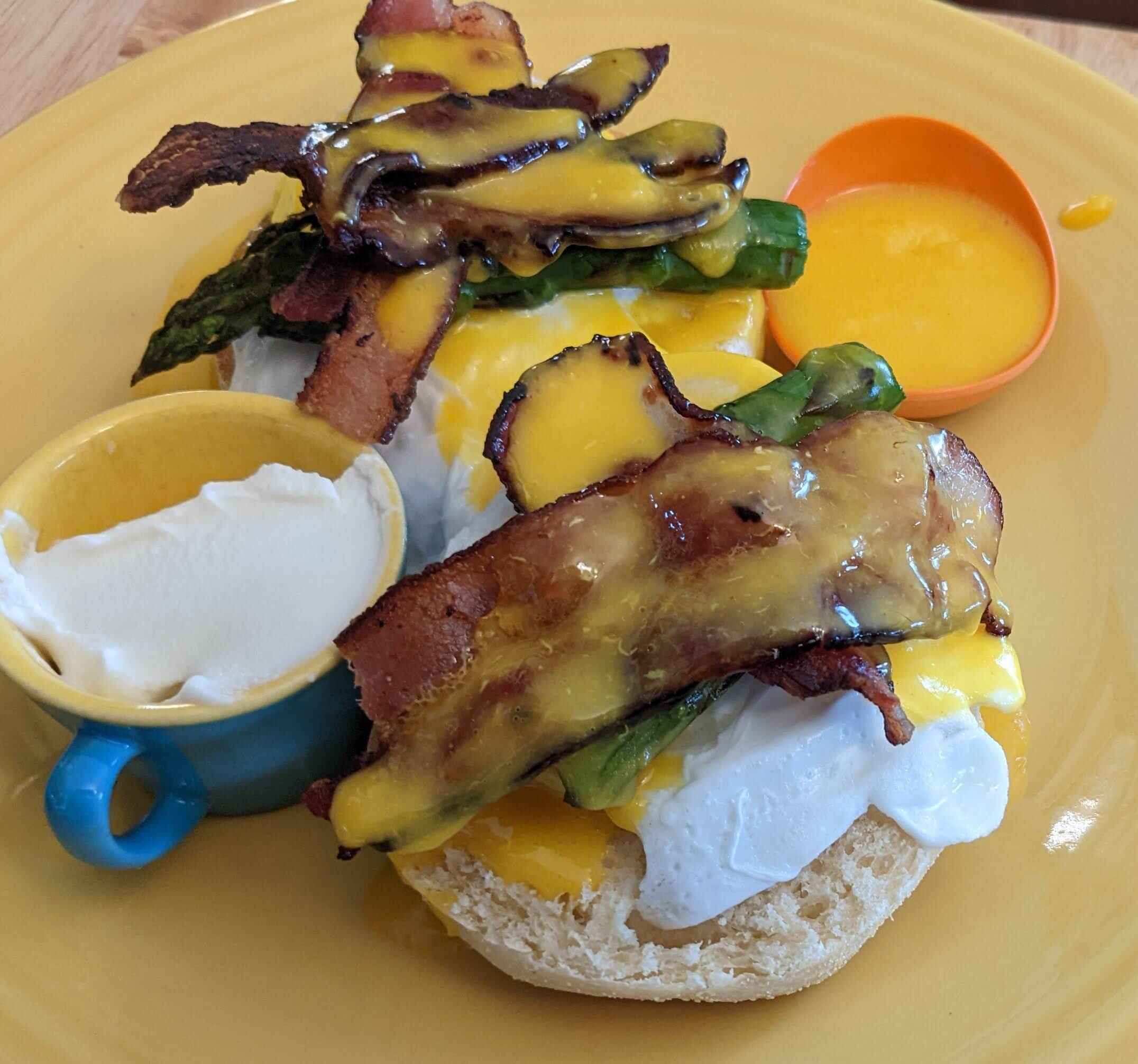 A breakfast plate with eggs Benedict, bacon, asparagus, and hollandaise sauce, served with a cup of coffee.