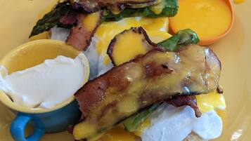 A breakfast plate with eggs Benedict, bacon, asparagus, and hollandaise sauce, served with a cup of coffee.