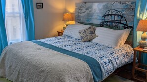 A bedroom with a bed, a headboard with a birdcage design, a nightstand with a lamp, and a window with blue curtains.