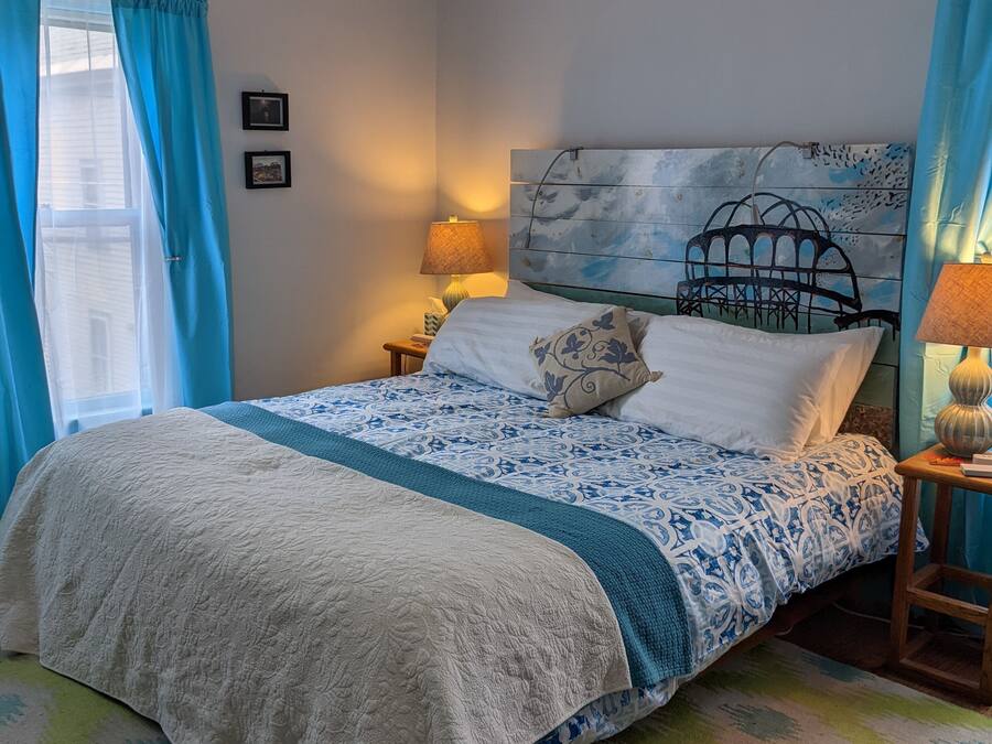 A bedroom with a bed, a headboard with a birdcage design, a nightstand with a lamp, and a window with blue curtains.