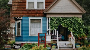 A blue house with a porch, a sign reading "The One Cat", and a garden with various plants and flowers.