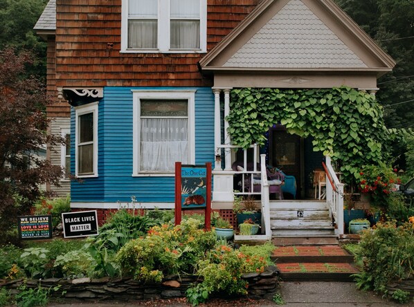 A blue house with a porch, a sign reading "The One Cat", and a garden with various plants and flowers. - The One Cat B&B (Brattleboro)
