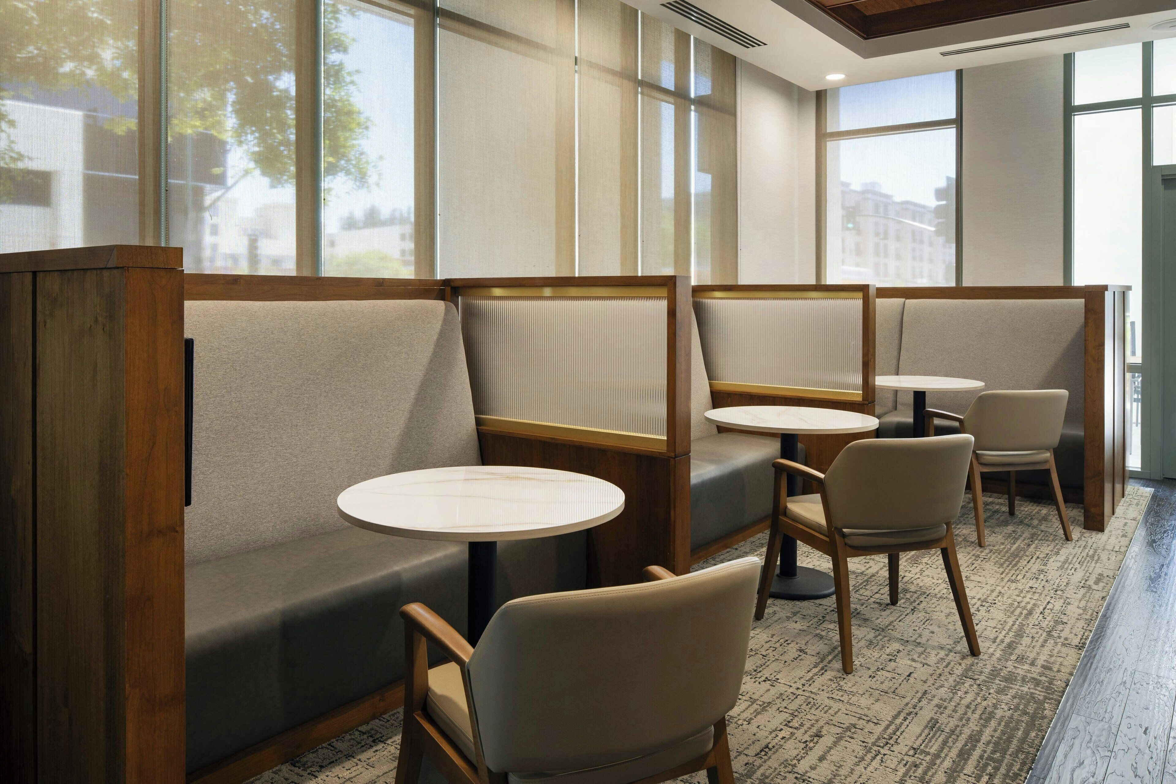 A modern hotel lobby with seating areas, large windows, and a carpeted floor.