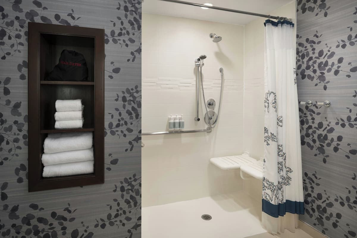 A bathroom with a shower, a towel rack with folded towels, and a shelf with toiletries.