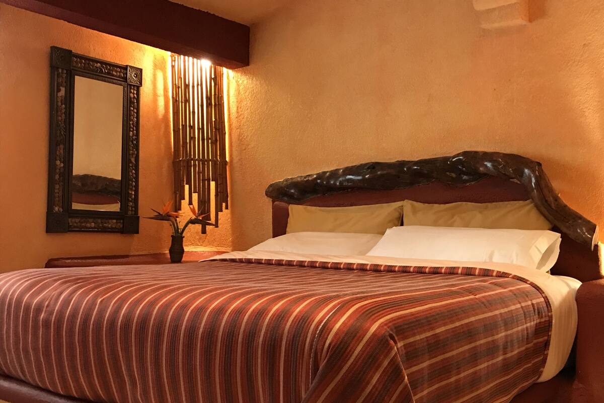A neatly made bed with striped bedding, a wooden headboard, and a wall-mounted mirror.