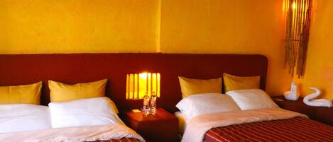 A hotel room with two beds, each with white linens and striped red bedding. There is a nightstand with a lamp and two bottles of water. The walls are painted yellow, and there is a decorative wall hanging with swans.