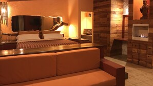Una habitación acogedora con una cama, un banco de madera, una chimenea y un espejo.