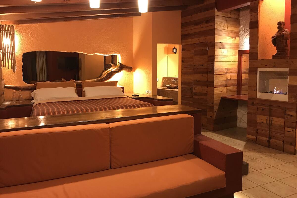 A cozy room with a bed, a wooden bench, a fireplace, and a mirror.
