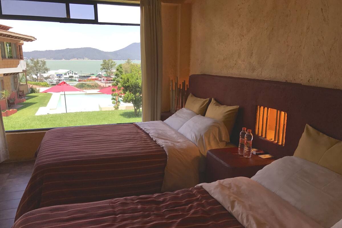 A hotel room with two beds, a view of a pool and mountains, and a window with curtains.