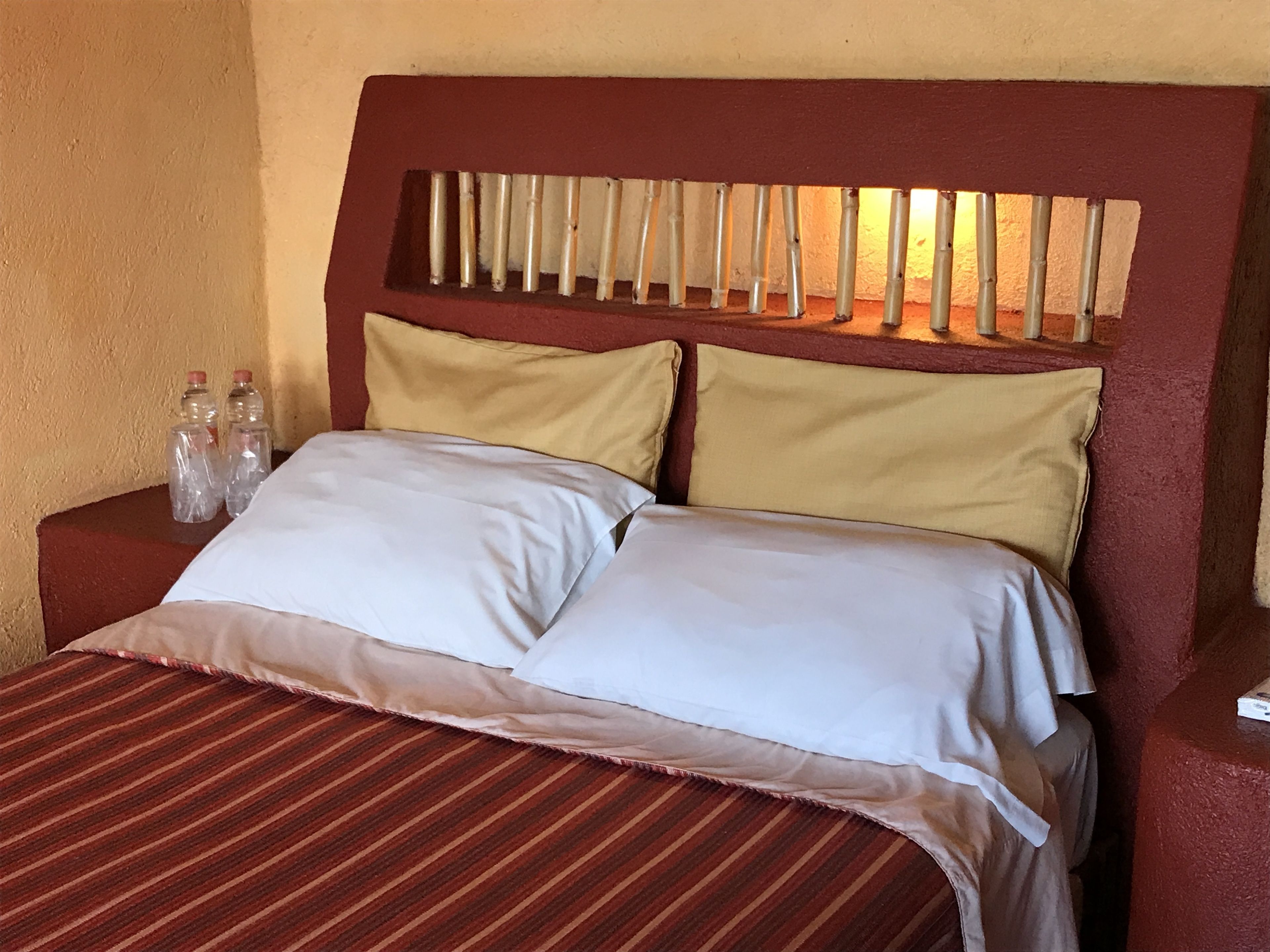 Una cama con colcha a rayas, dos almohadas y un cabecero con listones verticales.