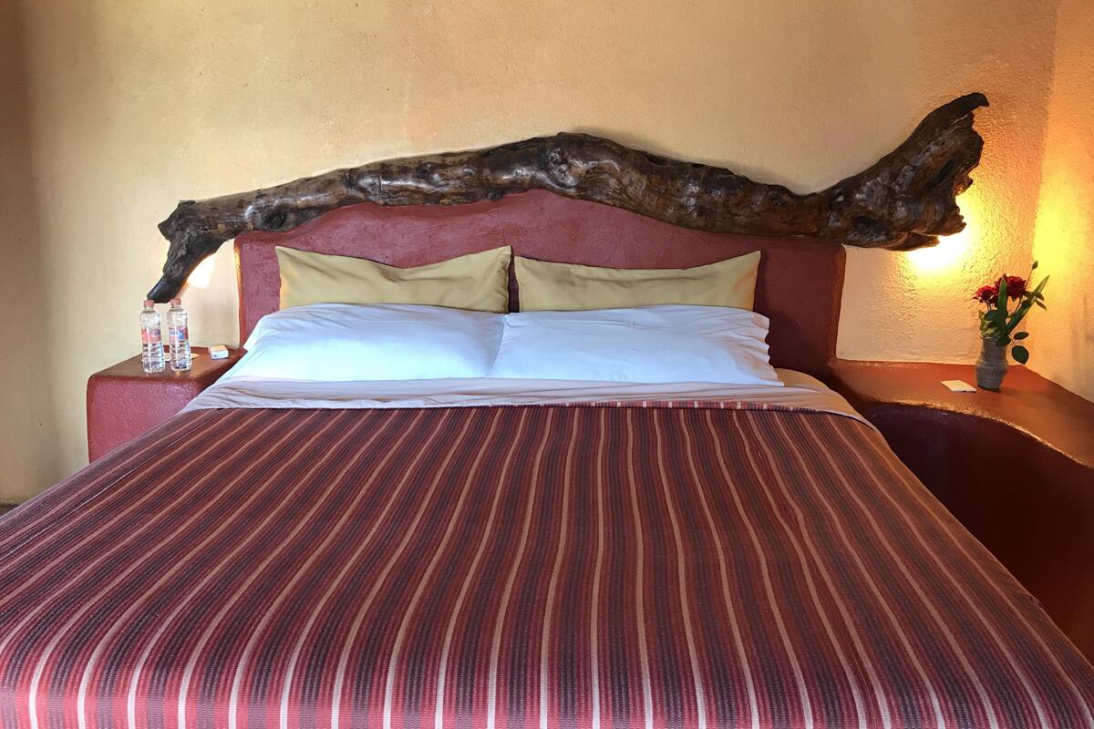 A bed with a red and white striped bedspread, two pillows, a wooden headboard, a nightstand with a vase of flowers, and a water bottle.