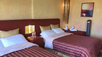 A hotel room with two beds, each with striped bedding, a nightstand with water bottles, a wall-mounted heater, and a framed picture on the wall.