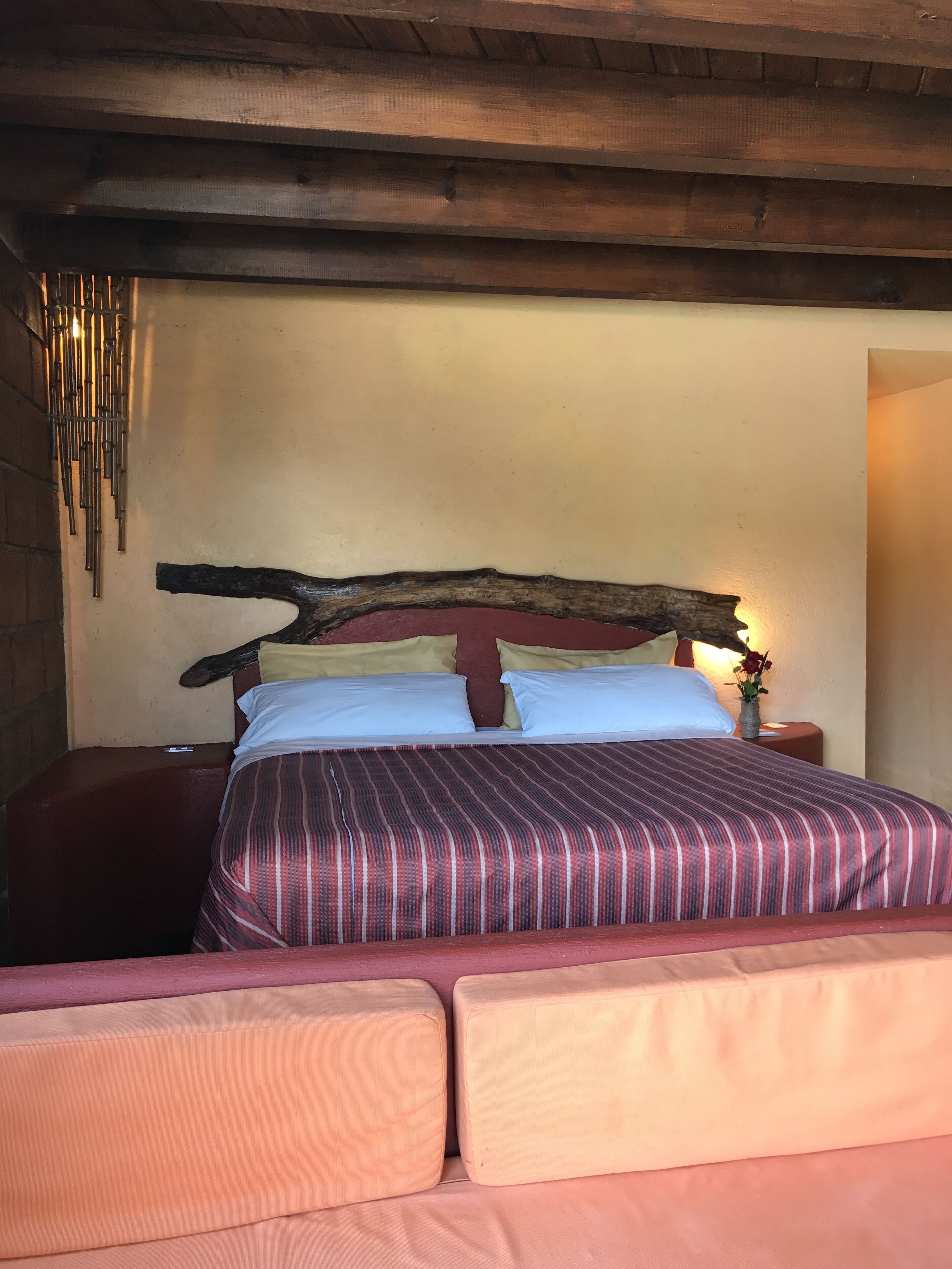 A bed with a wooden headboard, striped bedding, and a bedside table with a vase.