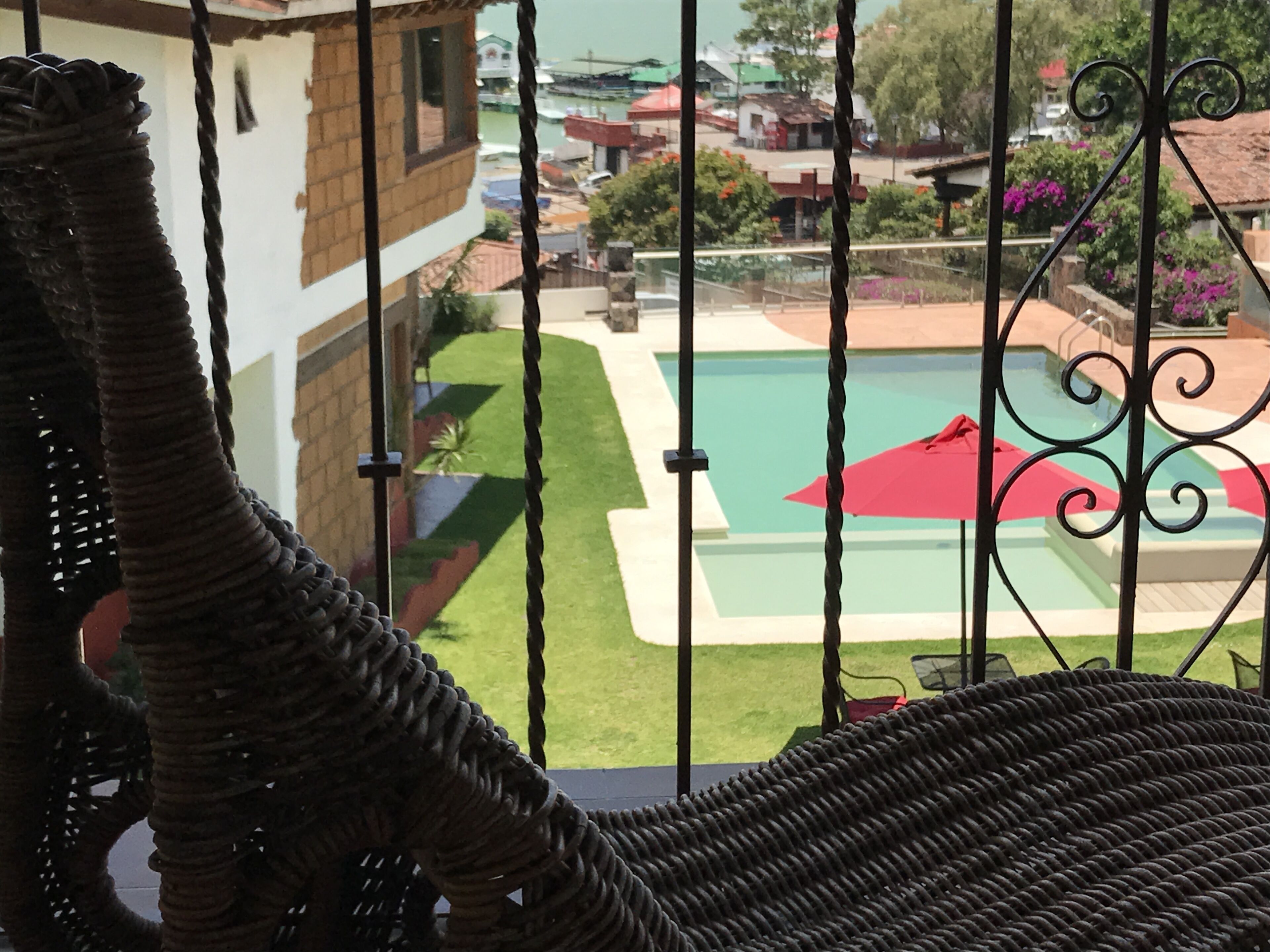 A view from a balcony with a wicker chair, a swimming pool, and a garden.