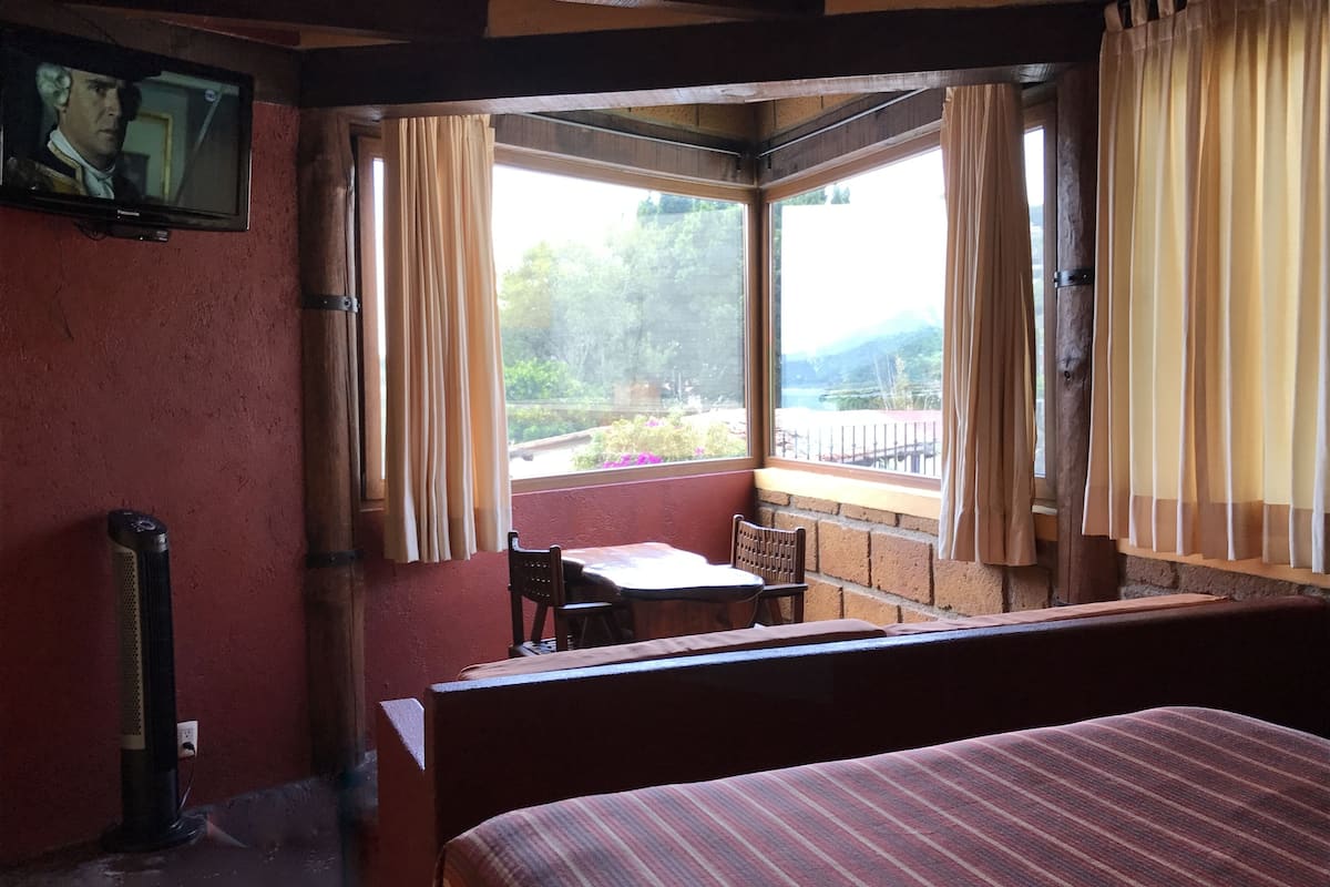 A room with a bed, a table, and a chair near a window with curtains.