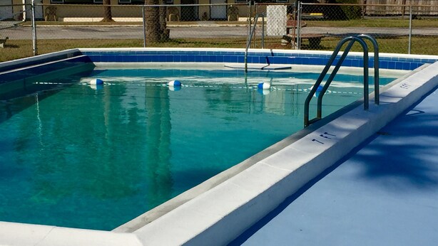 Une piscine rectangulaire dont l’intérieur est revêtu de carreaux bleus et dont le bord est blanc. On y trouve deux échelles métalliques, situées sur le côté droit.