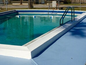 En rektangulär swimmingpool med blå kakelplattor på insidan och en vit kant. Det finns två metallstegar på höger sida.