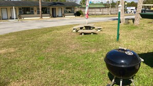 Un espace verdoyant équipé d’un barbecue, de tables de pique-nique et d’un bâtiment sur lequel est affiché un panneau indiquant que des repas du petit-déjeuner, du déjeuner et du dîner y sont servis.