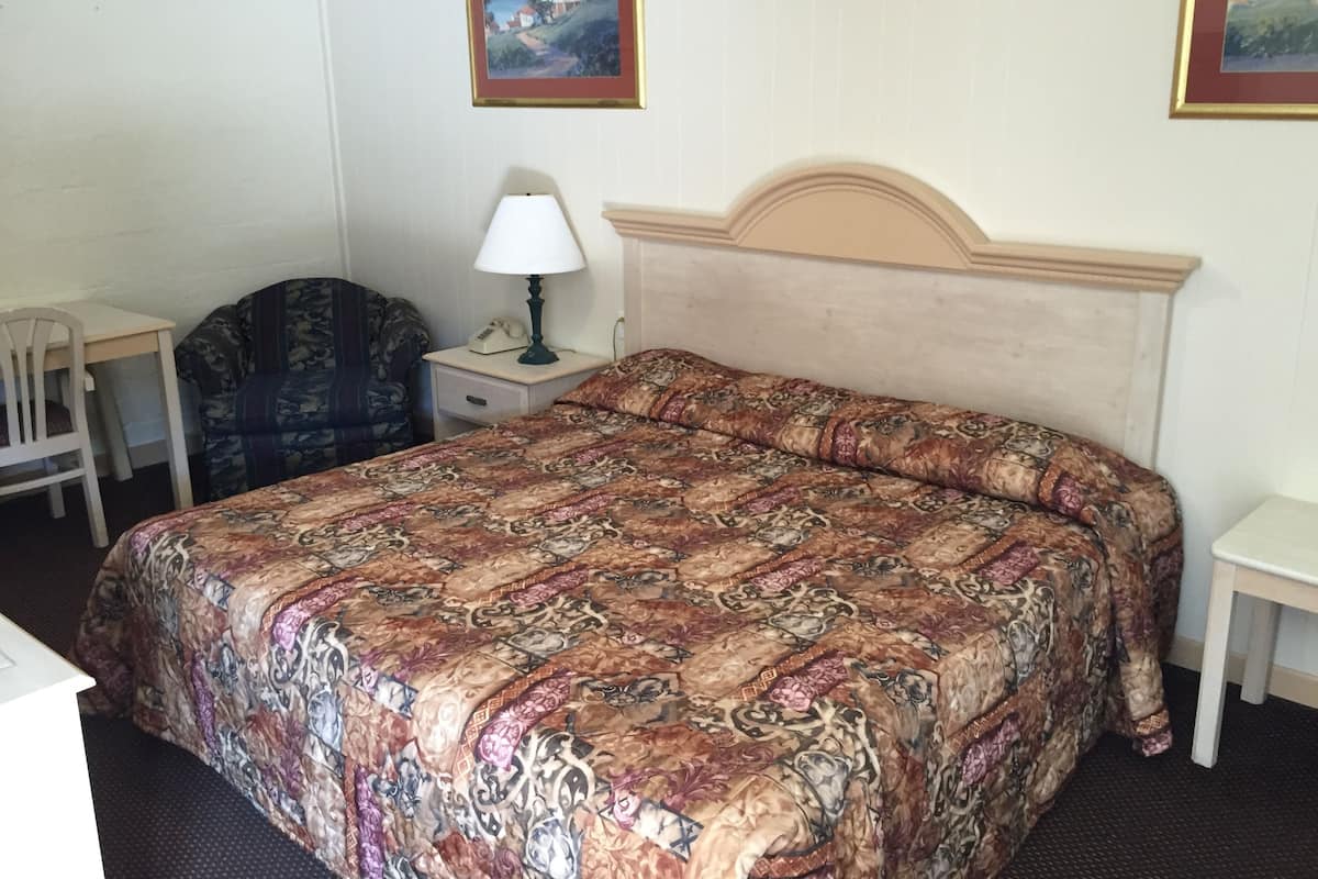 Un dormitorio con una cama grande, un escritorio, una silla y dos cuadros en la pared.