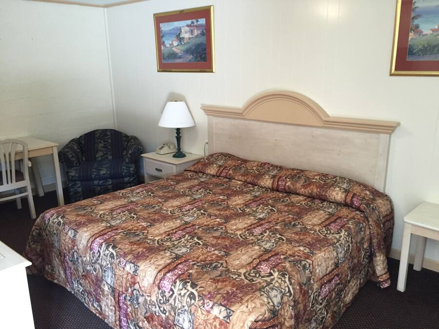 A bedroom with a large bed, a desk, a chair, and two paintings on the wall.