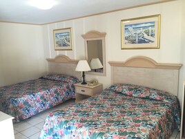 Habitación de hotel con dos camas, cada una con ropa de cama floral, una mesita de noche con lámpara y dos cuadros en la pared.