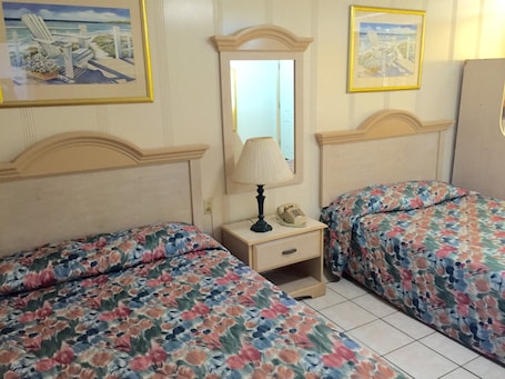 A bedroom with two beds, a bedside table with a lamp and a telephone, and a mirror on the wall.