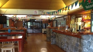 Een bar met een stenen toonbank, houten tafels en een zithoek met banken.