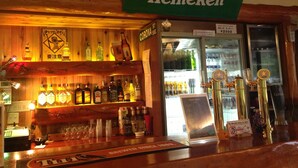 Een bar met een Heineken bord, verschillende drankflessen en een bierkraan.
