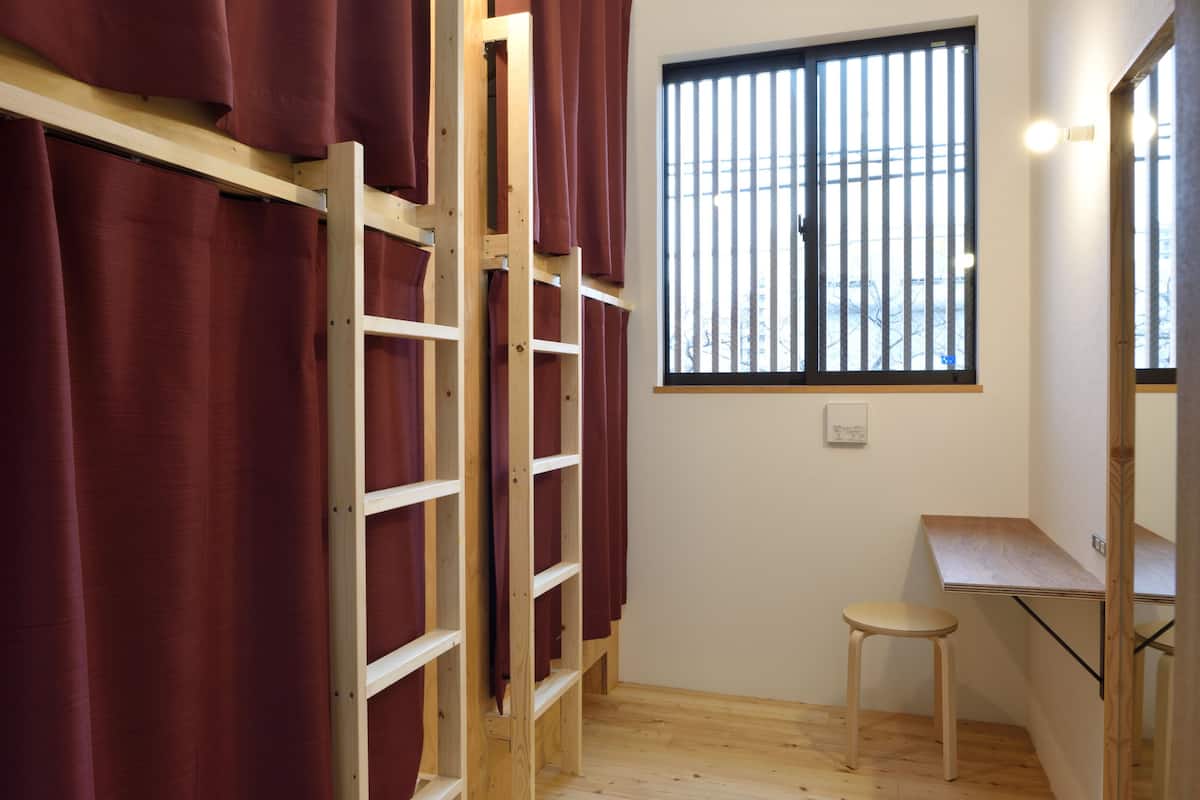 A room with a wooden ladder, a window with bars, a stool, and a desk.