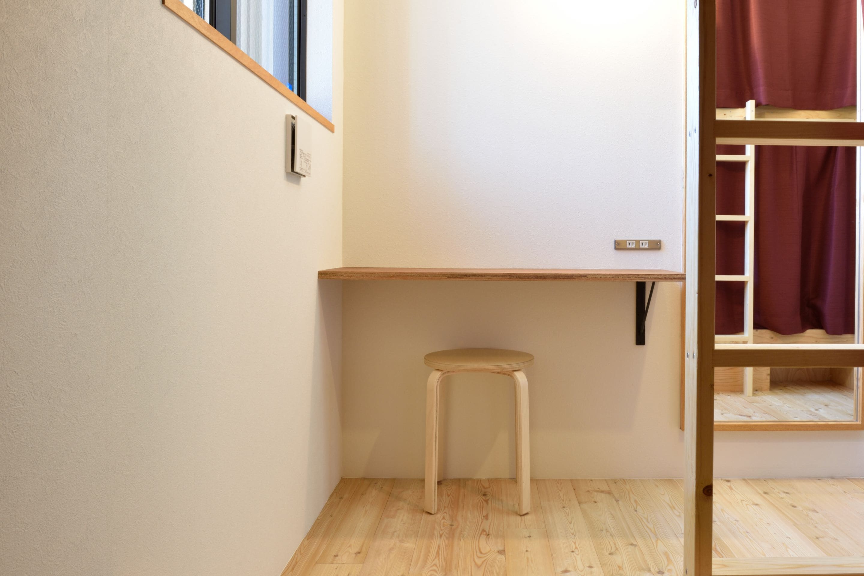 Una habitación con escritorio de madera, un taburete y una cama litera con ventana.